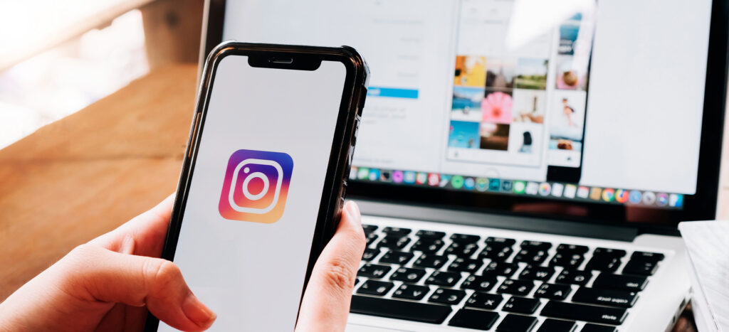 Logo de instagram en la pantalla del celular y un computador de fondo en la página de instagram web